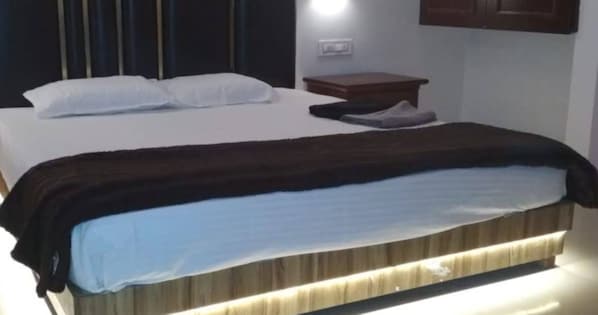A neatly made bed with a dark headboard, a bedside table with a lamp, and a wall-mounted light fixture. - H2O Valley lgatpuri (Igatpuri)