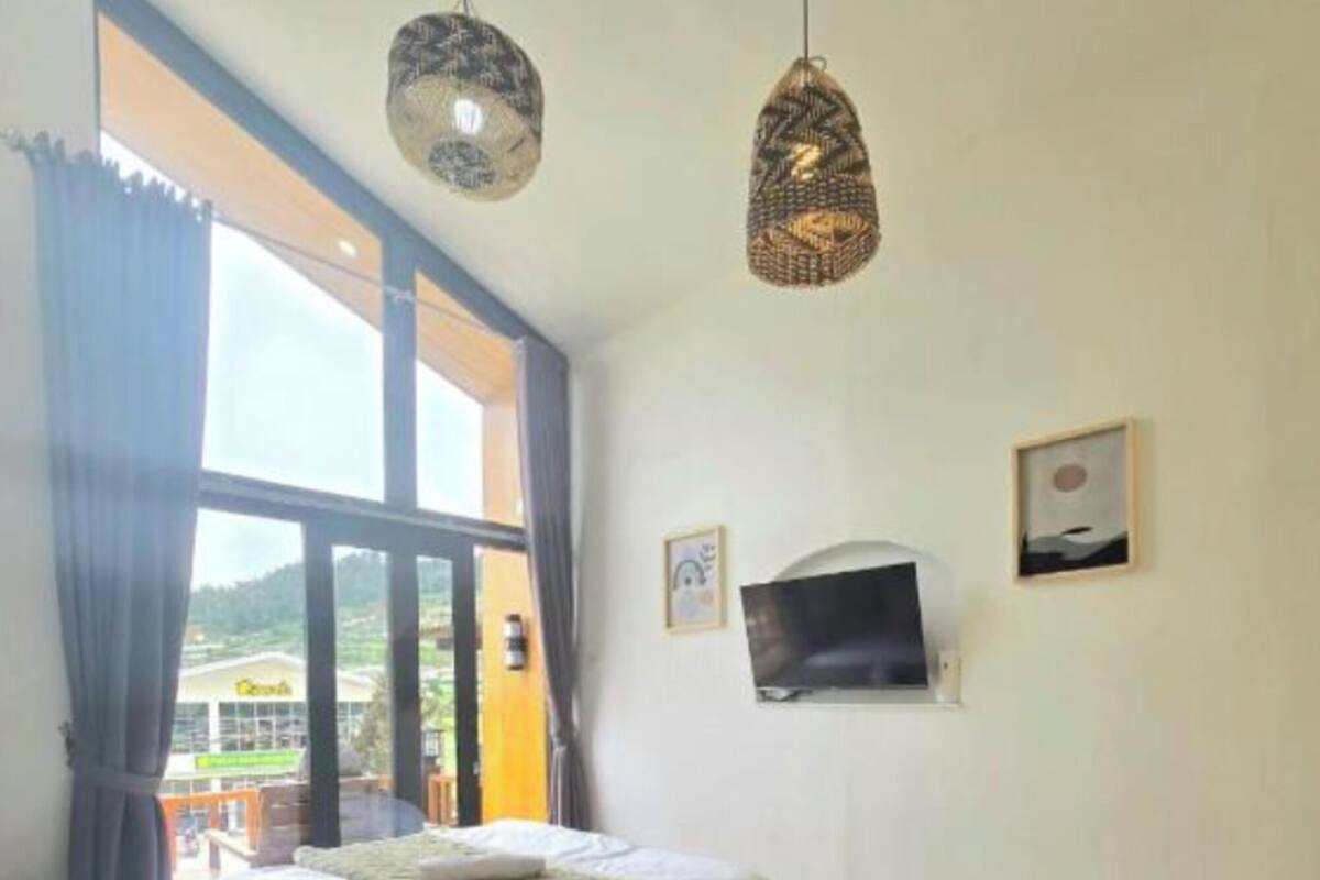 Un dormitorio con una cama, un televisor en la pared y una ventana con cortinas.