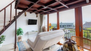A room with a sofa, a television, a window with a view, and a staircase. - Linggayoni Cottage Dieng (Dieng Kulon)