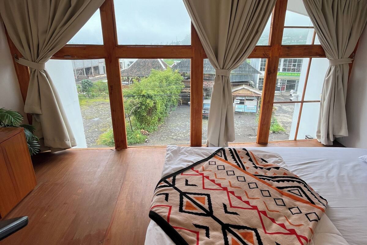 Un dormitorio con una cama grande, suelo de madera y vistas a través de una ventana con cortinas.