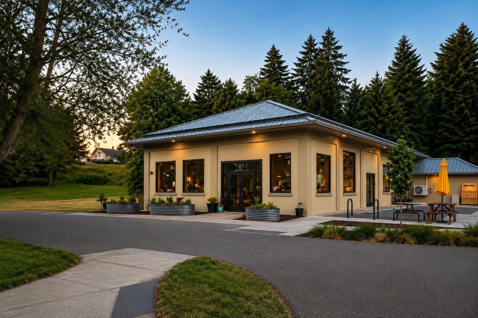 A small, single-story building with a flat roof, large windows, and a paved entrance area with a bench.