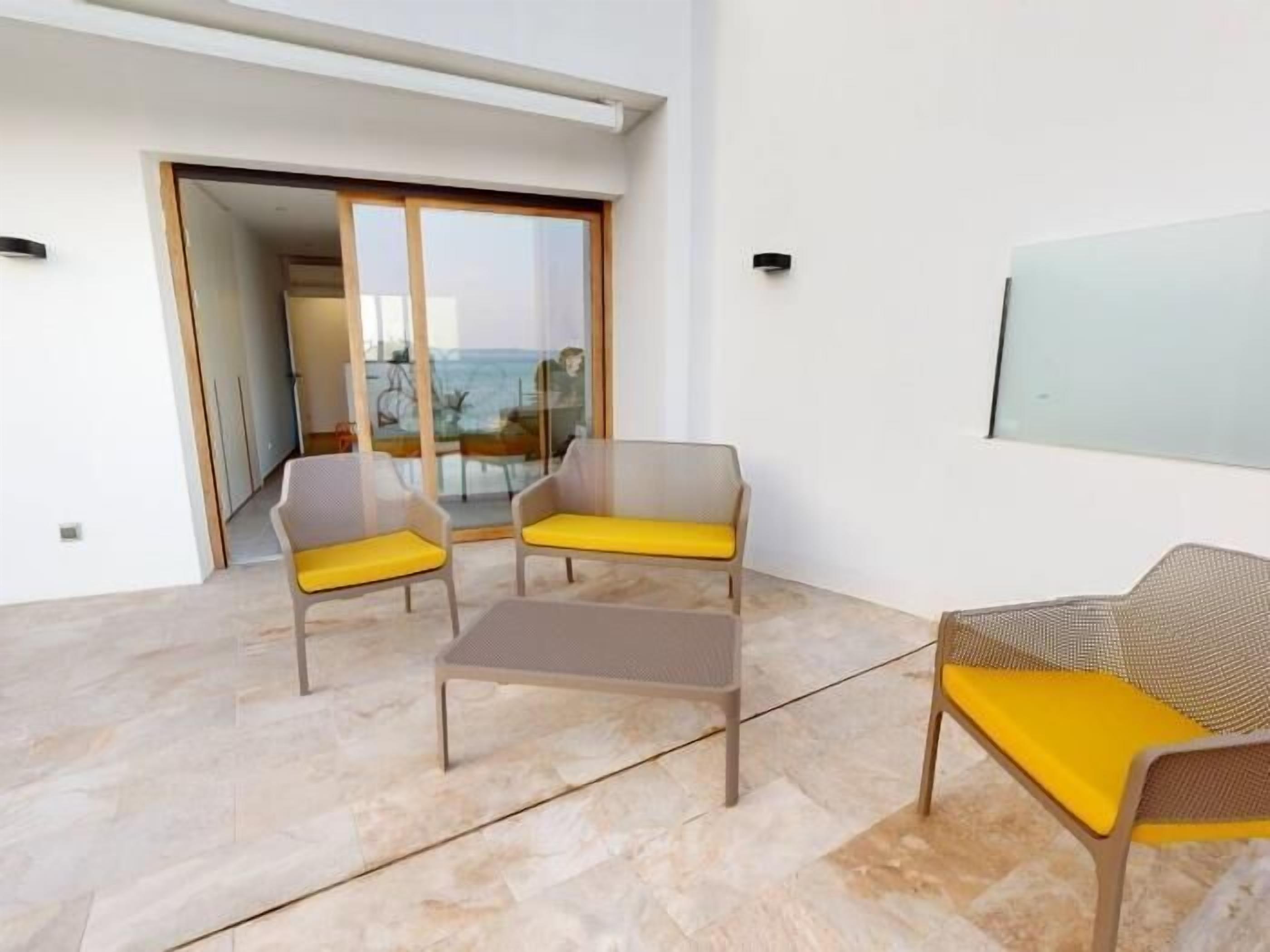 Una sala de estar moderna con un ventanal que da a un balcón, dos sillones con cojines amarillos y una mesita.