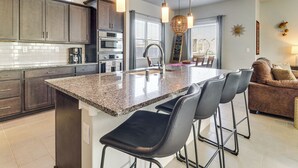 Una cocina moderna con encimeras de granito, electrodomésticos de acero inoxidable y una isla central con taburetes de bar.