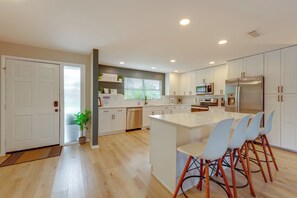 Una cocina moderna con armarios blancos, una isla central con sillas, lavavajillas y refrigerador.