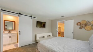 Un dormitorio con cama, puerta corredera al baño, televisor en la pared y un adorno decorativo en la pared.