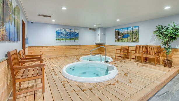 Una terraza de madera con dos jacuzzis, bancos de madera y una planta en maceta.