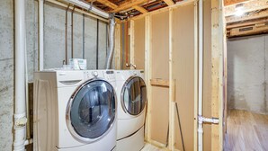 A laundry room with two stacked front-loading washing machines, wooden walls, exposed ceiling with electrical wiring, and a wooden floor. - Angler's Retreat 1 Block to Lake Winneconne (Winneconne)