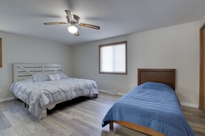 Une chambre avec deux lits, un ventilateur de plafond, une fenêtre avec des stores et un plancher en bois.