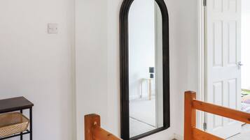 A room with a wooden-framed mirror, a small table with a basket, and a door leading to another space.