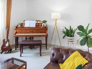 A living room with a piano, a guitar, a bench, a sofa, a floor lamp, and potted plants. - 3 bedroom accommodation in Uckfield (Uckfield)