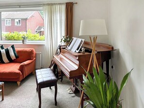 A living room with a piano, a sofa, a bench, and a lamp.