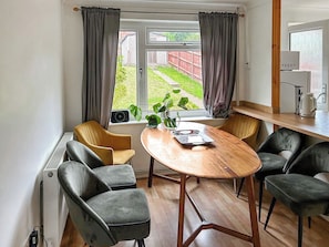 A modern dining area with a wooden table and chairs, a view of a garden through a window, and a kitchen area with appliances. - 3 bedroom accommodation in Uckfield (Uckfield)