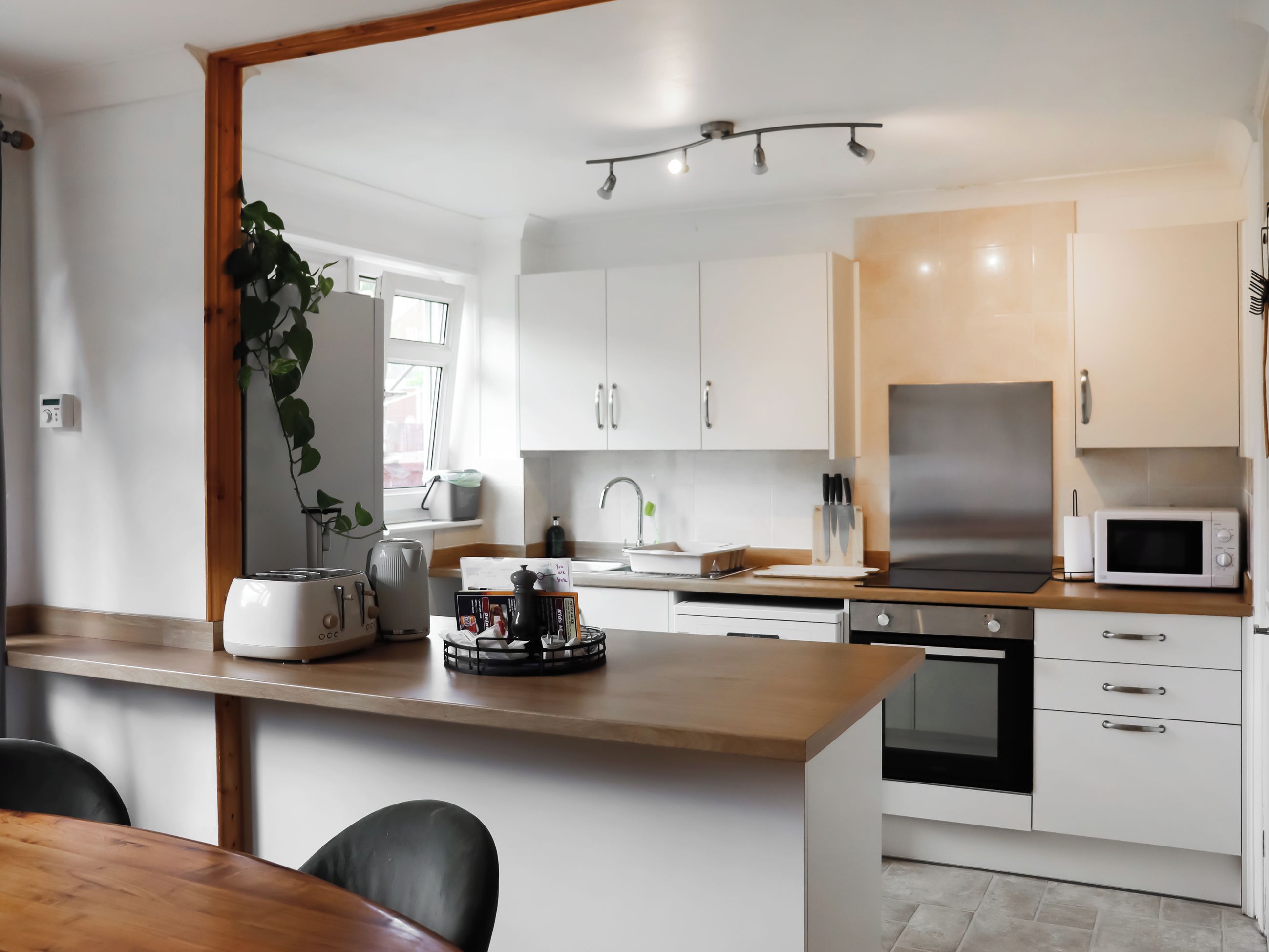 Eine moderne Küche mit weißen Schränken, einer Holz Arbeitsplatte, einem Edelstahl-Kühlschrank und einer Mikrowelle.