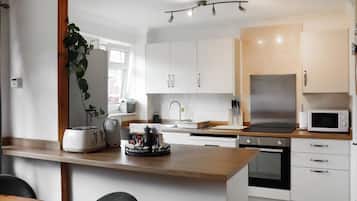 A modern kitchen with white cabinets, a wooden countertop, a stainless steel refrigerator, and a microwave.