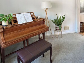 A wooden piano with sheet music, a bench, a floor lamp, and two potted plants in a room with a carpeted floor.