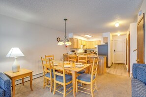 Un coin repas avec une table et des chaises en bois, une lampe, et une cuisine en arrière-plan.