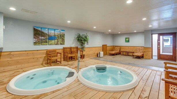 Ein Wellnessbereich mit zwei Whirlpools, Holzboden, Sitzgelegenheiten und einem Gemälde an der Wand.