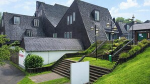 A residential building with a steeply pitched roof, a reception area, and a staircase leading to the entrance. - Nature Stay in Hambachtal Holiday Park (Oberhambach)