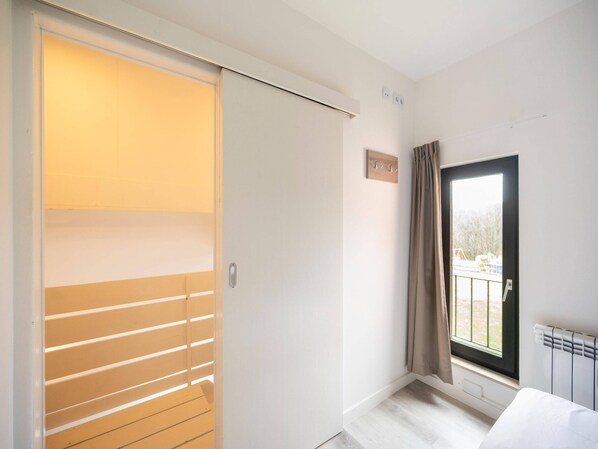 Una habitación con puerta corredera, un radiador, una ventana con cortinas y un pequeño cartel en la pared.