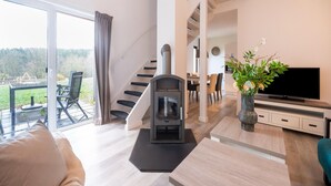 A modern living room with a fireplace, a dining area, and a staircase leading to an upper level. - Nature Stay in Hambachtal Holiday Park (Oberhambach)