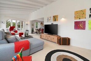 Ein modernes Wohnzimmer mit einem grauen Sofa, roten Sesseln, einem Fernseher und Kunstwerken an den Wänden.