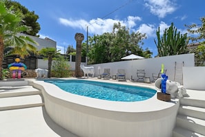 Ein Pool mit gewölbter Kante, umgeben von weißen Wänden und einigen Stühlen.