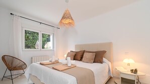 Ein ordentlich eingerichtetes Schlafzimmer mit einem großen Bett, einem Nachttisch mit Lampe und einem Sessel.