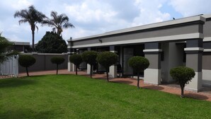 Un edificio moderno con techo plano, patio empedrado y setos cuidados.