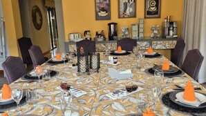 Comedor con una mesa larga dispuesta para varias personas, con mantel estampado, platos blancos y negros, y servilletas anaranjadas.