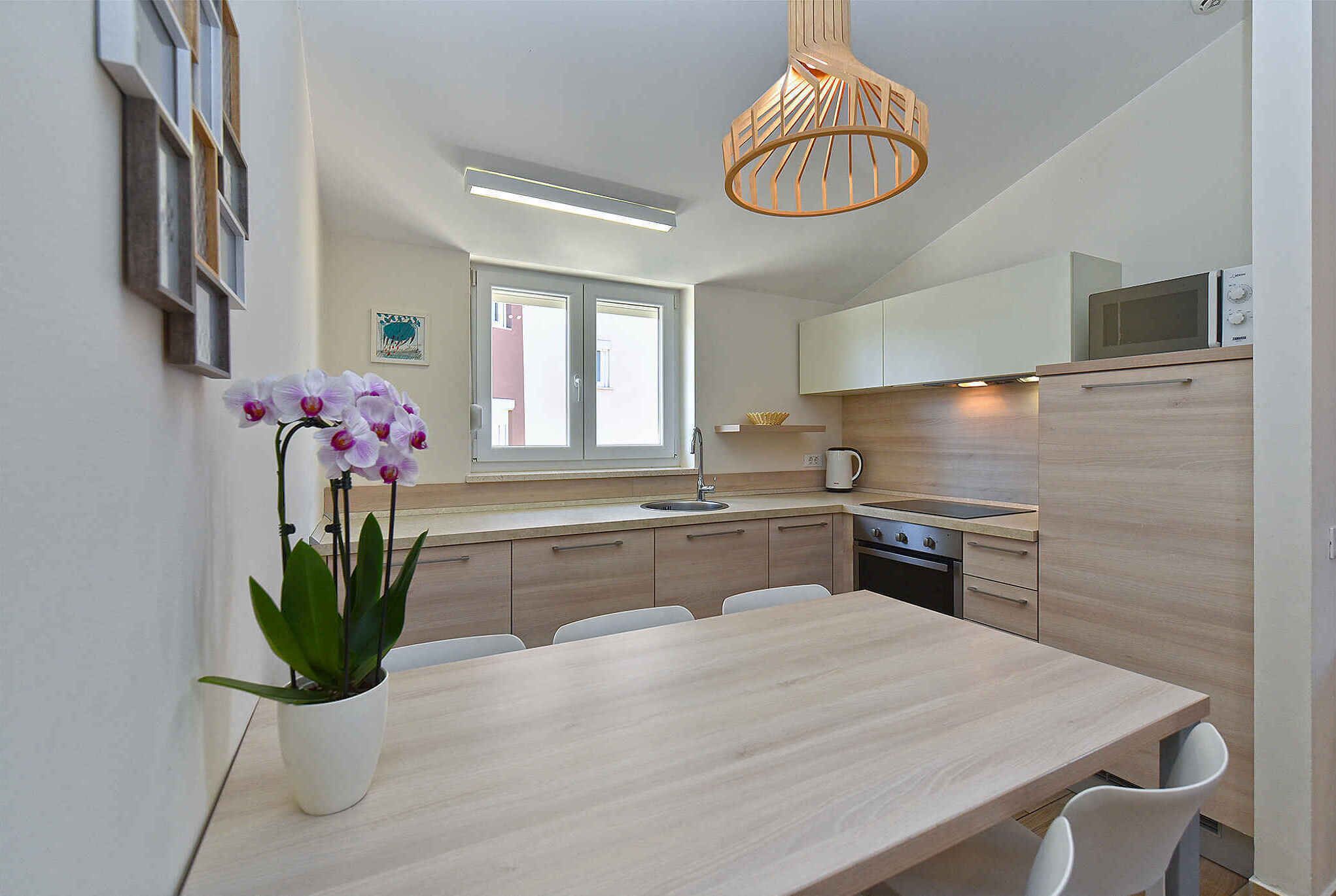 Une cuisine moderne avec une table en bois, des chaises blanches, une orchidée en pot et un luminaire suspendu.