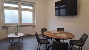 Ett modernt matområde med ett runt träbord, fyra stolar, ett litet sidobord med en växt och en stor platt-TV som är monterad på väggen.