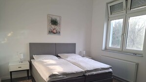 Ett sovrum med en dubbelsäng, ett nattduksbord med en lampa, ett element och ett fönster med persienner.