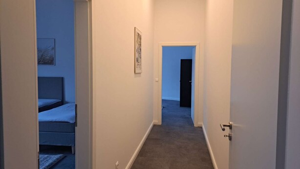 En smal hall med ett heltäckningsmatta på golvet, vita väggar och en dörr längst in som leder till ett annat rum.