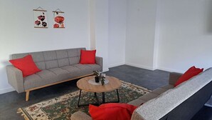 A living room with a grey sofa, red cushions, a round coffee table, and a floral rug. - Modern, spacious 3-room apartment - 85 m² (Solingen)