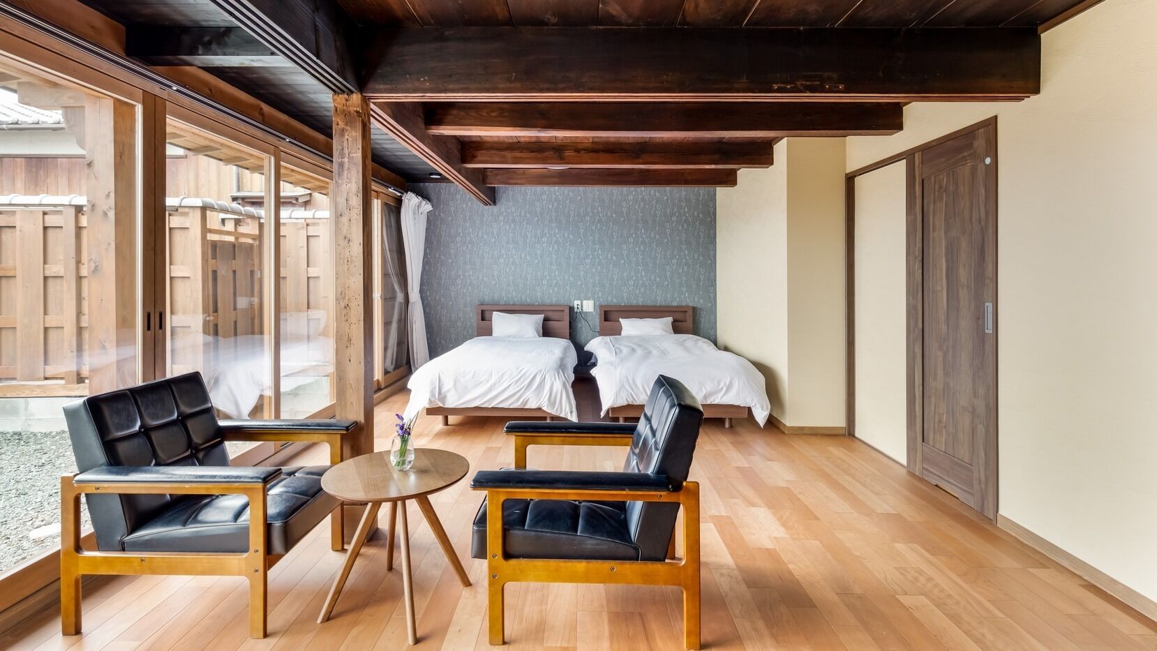 Habitación de hotel con dos camas, techo de madera, un ventanal grande y una pequeña mesa redonda con sillas.