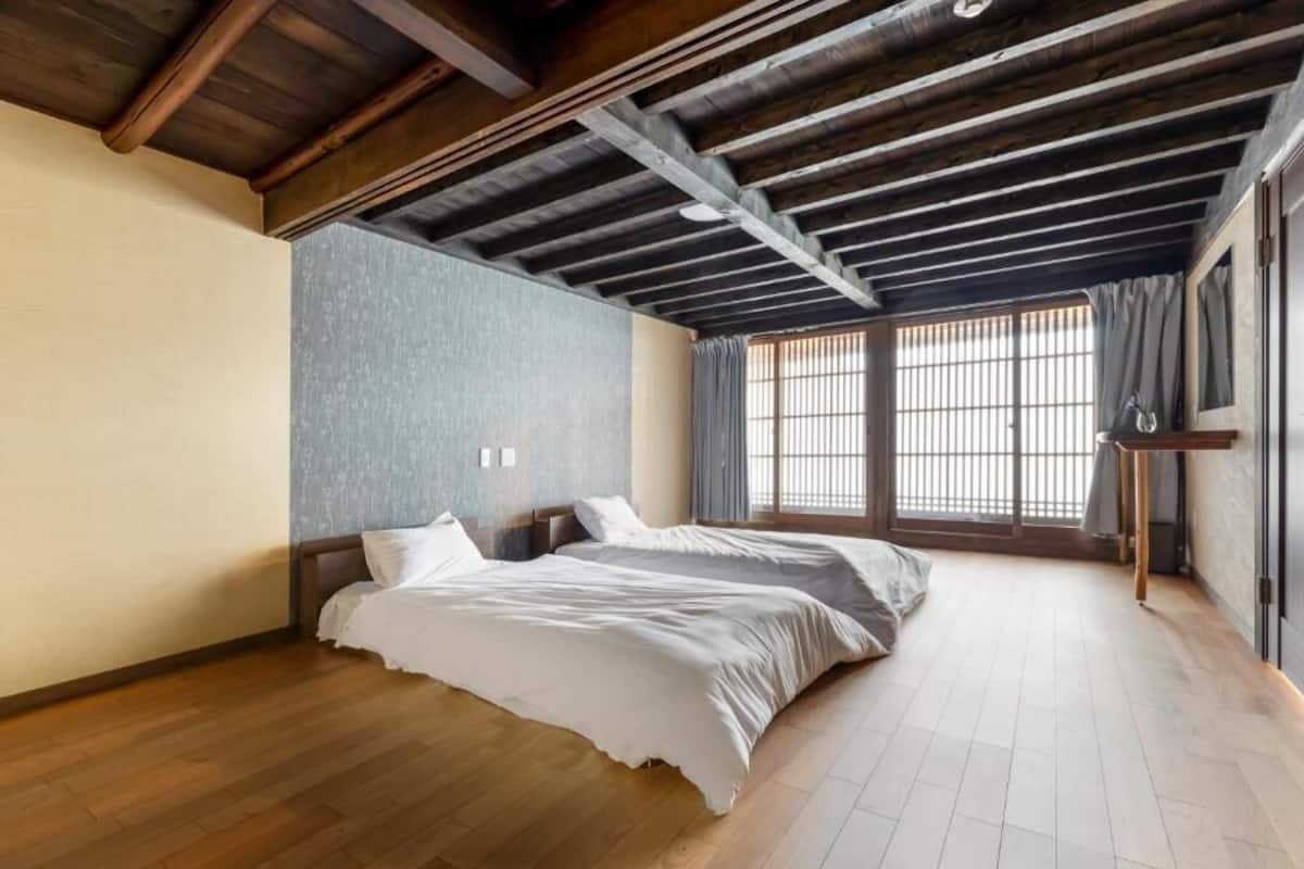 Una stanza con due letti, travi in legno a vista al soffitto, un'ampia finestra con tende e pavimento in legno.