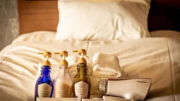 A neatly arranged set of toiletries on a bed with white linens, including shampoo, conditioner, body soap, and a toothbrush.