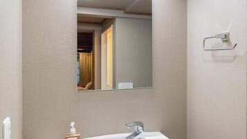 Un baño con lavamanos blanco, un espejo y una lámpara sobre el espejo.