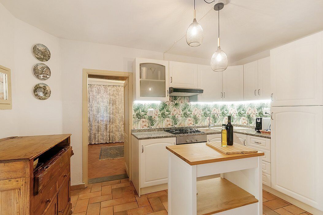 Una cocina compacta con armarios blancos, una isla central, una estufa a gas e iluminación colgante.