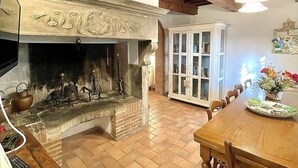 Eine traditionelle Küche mit einem Kamin aus Stein, Holzbalken und einem Essbereich mit Tisch und Stühlen.