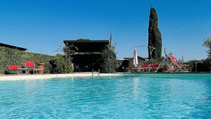 Ein Swimmingpool mit roten Liegestühlen und ein hoher Baum im Hintergrund.