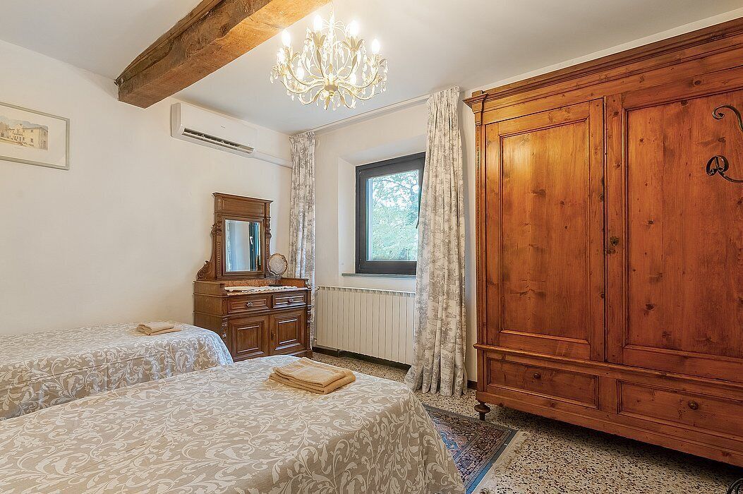 Et soveværelse med to senge, et træskab, en lysekrone og et vindue med gardiner.