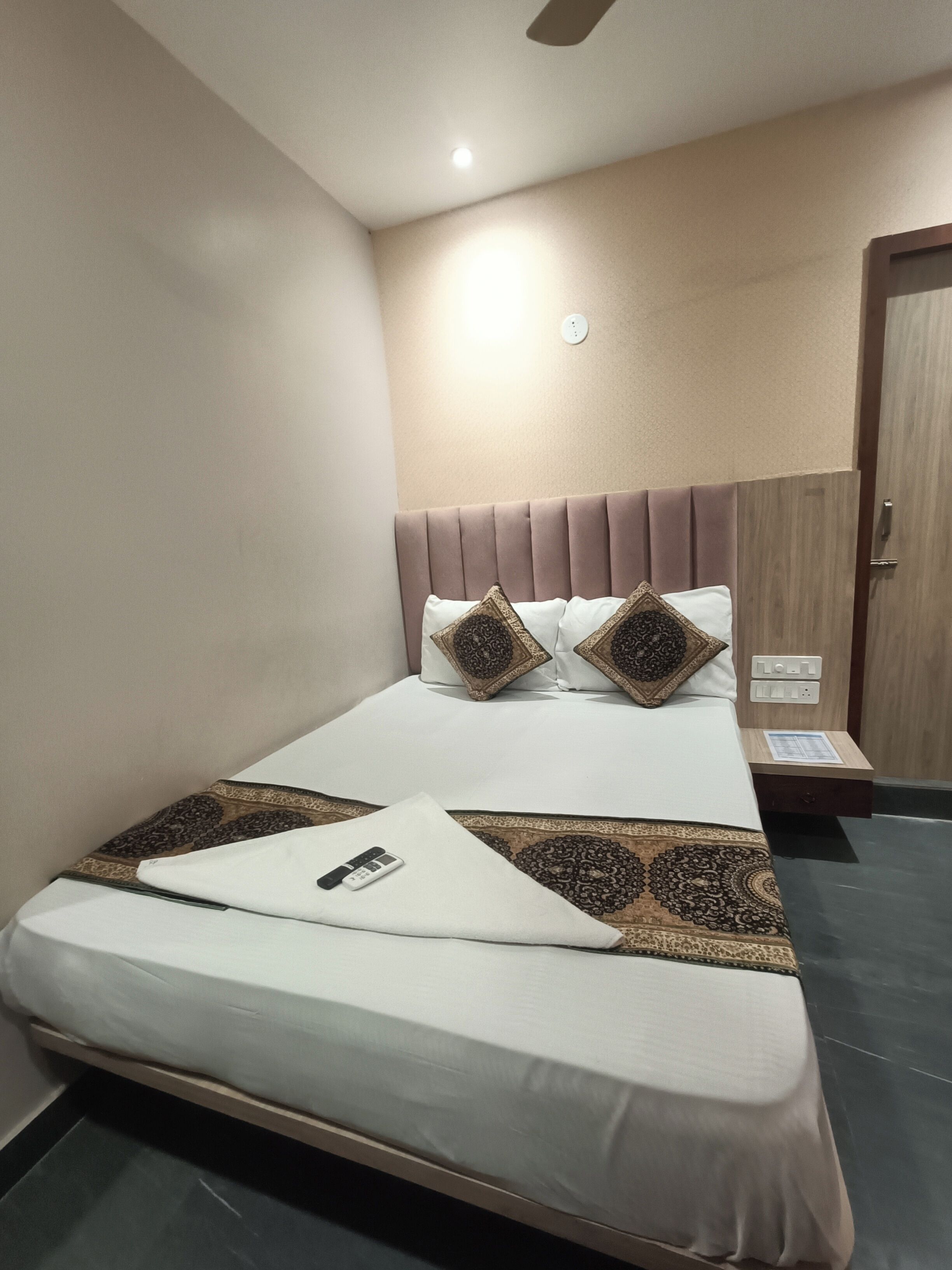 A neatly made bed with a remote control, a patterned rug, and a wooden headboard.
