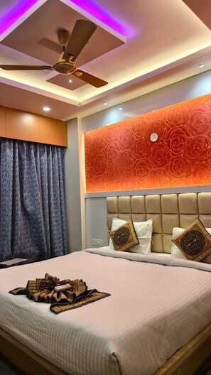 A bedroom with a bed, a ceiling fan, a wall with a floral pattern, and a window with curtains. - Hotel Radha Rani Palace (Puri)