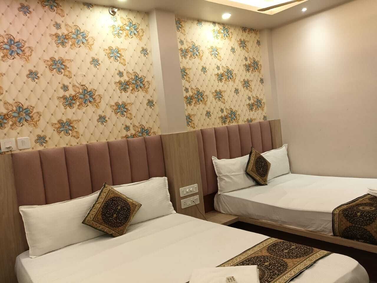 Habitación de hotel con dos camas, cada una con cabecera y almohadas. La habitación tiene papel tapiz estampado y piso de color claro.