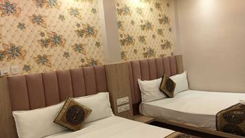 Habitación de hotel con dos camas, cada una con cabecera y almohadas. La habitación tiene papel tapiz estampado y piso de color claro.