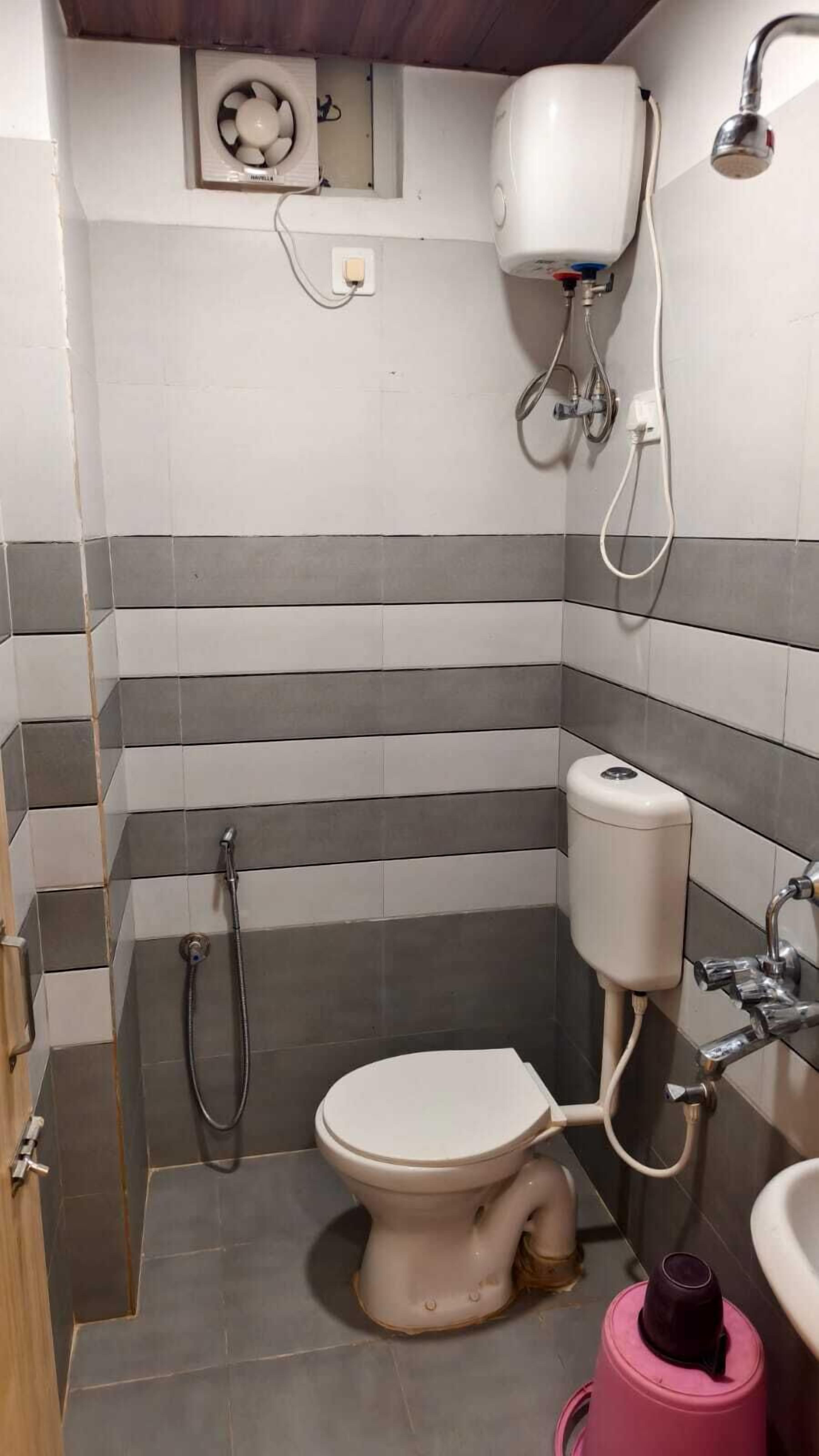 A small, narrow bathroom with a toilet, a shower, and a toilet paper holder.
