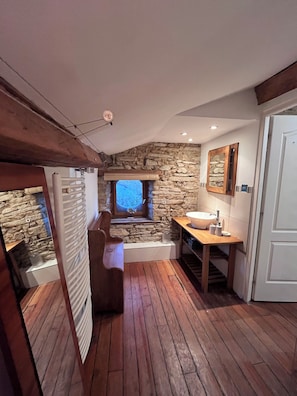 A compact bathroom with a stone wall, a wooden bench, a sink, and a window with a view.
