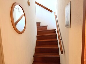 Eine Holztreppe mit Handlauf, ein runder Spiegel und ein gerahmtes Bild an der Wand.