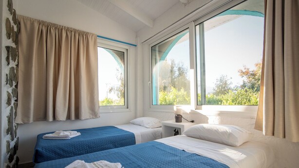 Una habitación con dos camas, una ventana que da a zonas verdes y una mesita de noche con una lámpara.